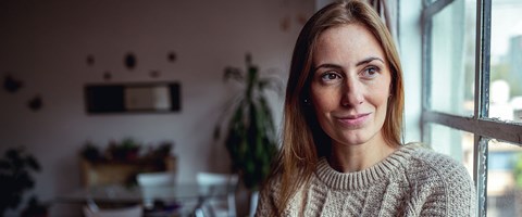 kvinne i 30-årene står ved vinduet og tenker.